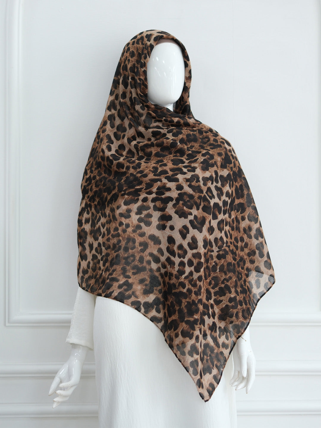 A leopard print headscarf draped over a white mannequin against a white paneled wall.