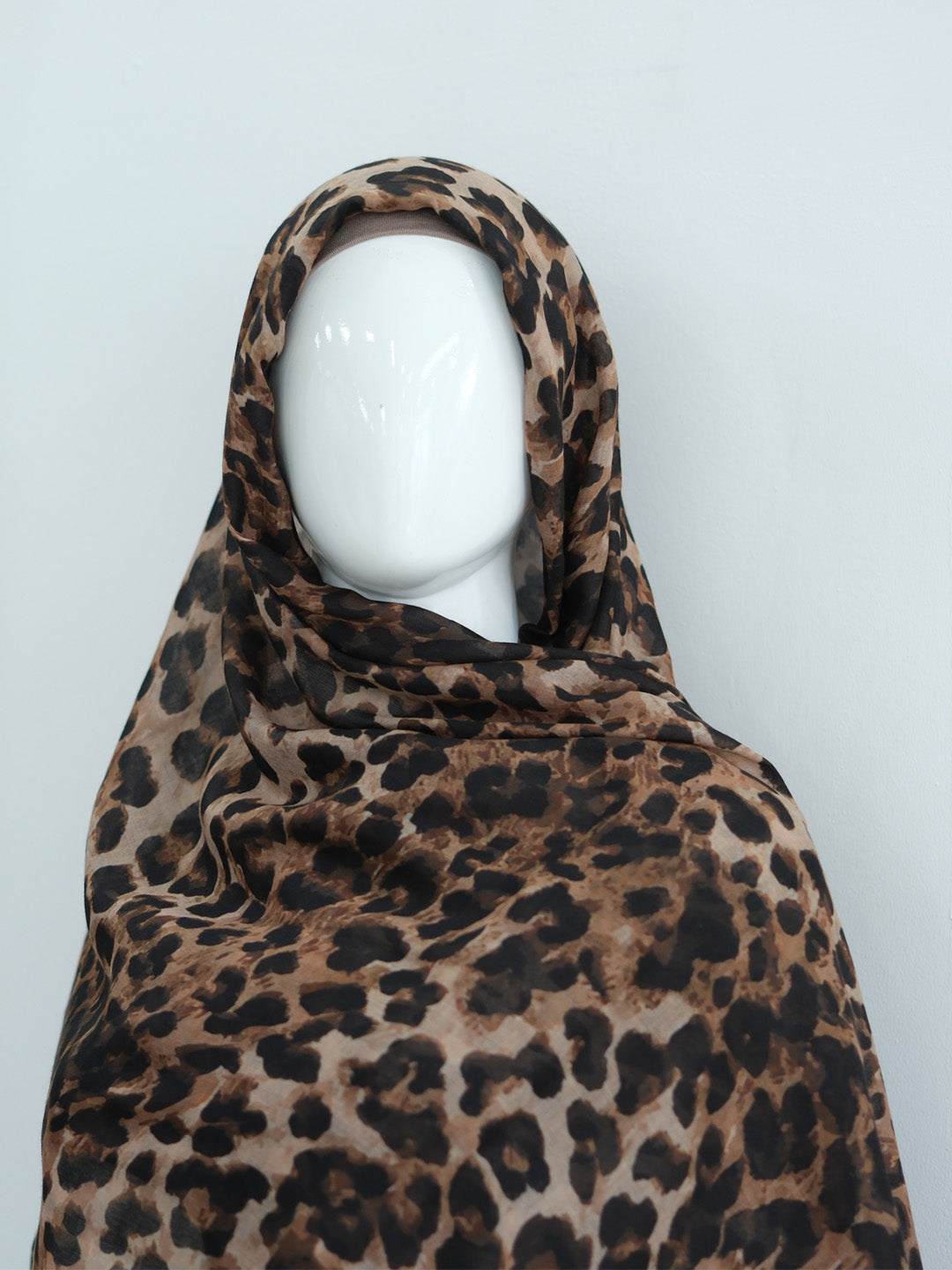 A leopard print headscarf draped on a white mannequin head, set against a plain light gray background.