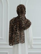 A leopard print hijab draped over a mannequin wearing a white dress, shown from the back against a white paneled wall.