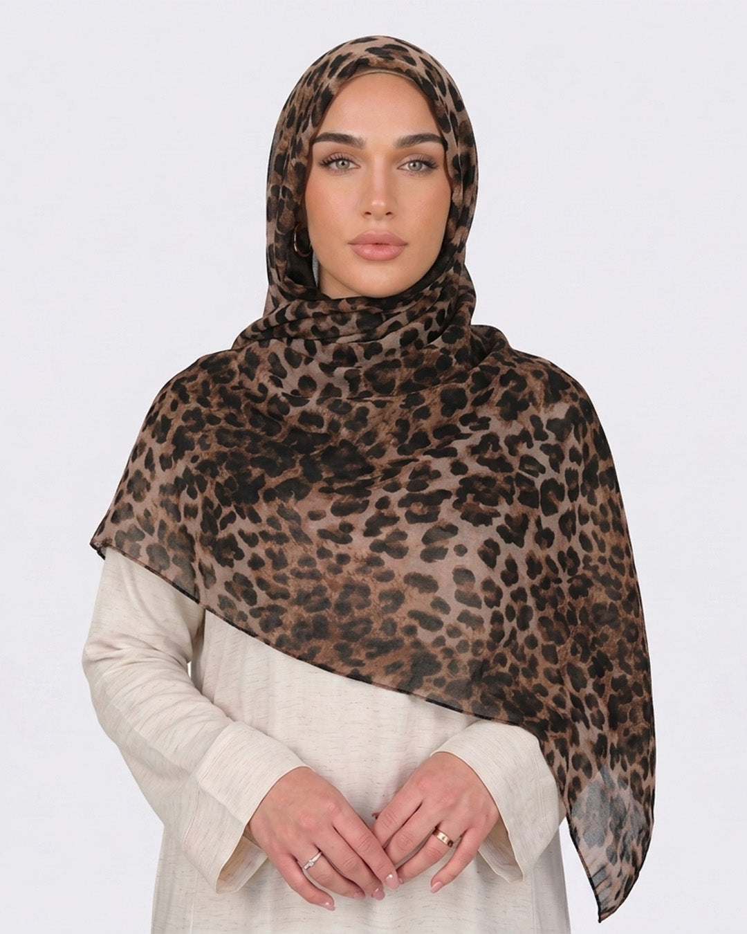 A woman wearing a classic leopard print modal hijab with warm tan, camel, and deep black rosettes, paired with a cream shirt dress.