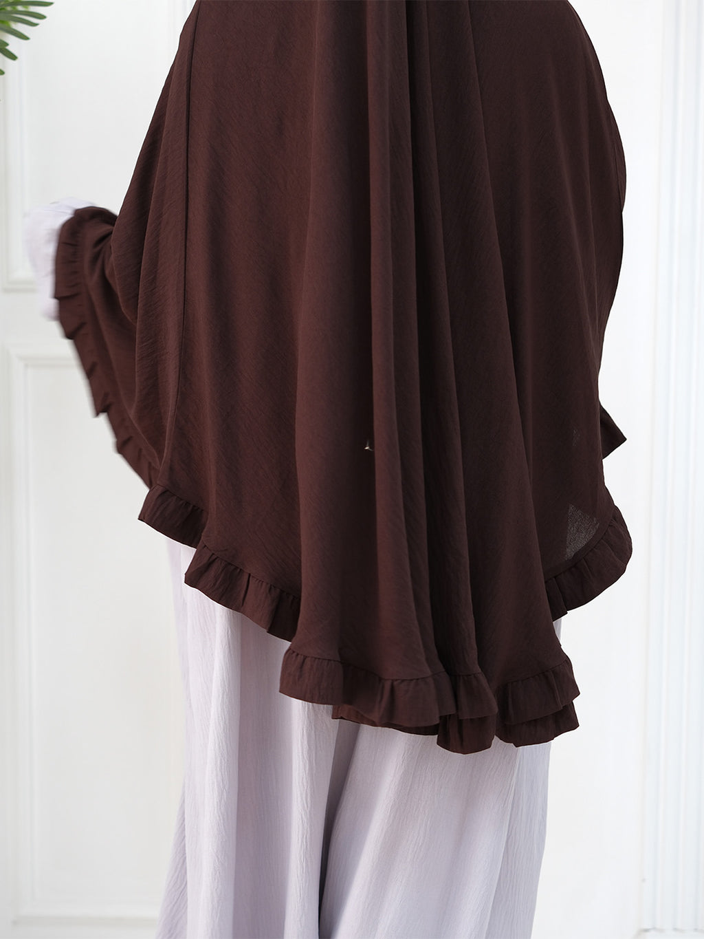 A dark brown sheer chiffon shawl or wrap with ruffled edges, worn over white trousers.