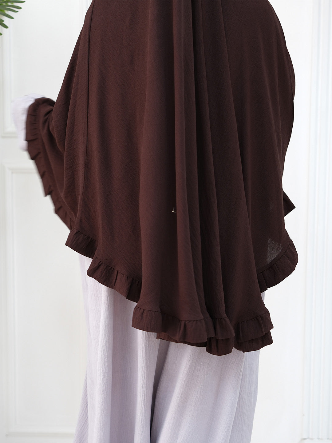 A dark brown sheer chiffon shawl or wrap with ruffled edges, worn over white trousers.
