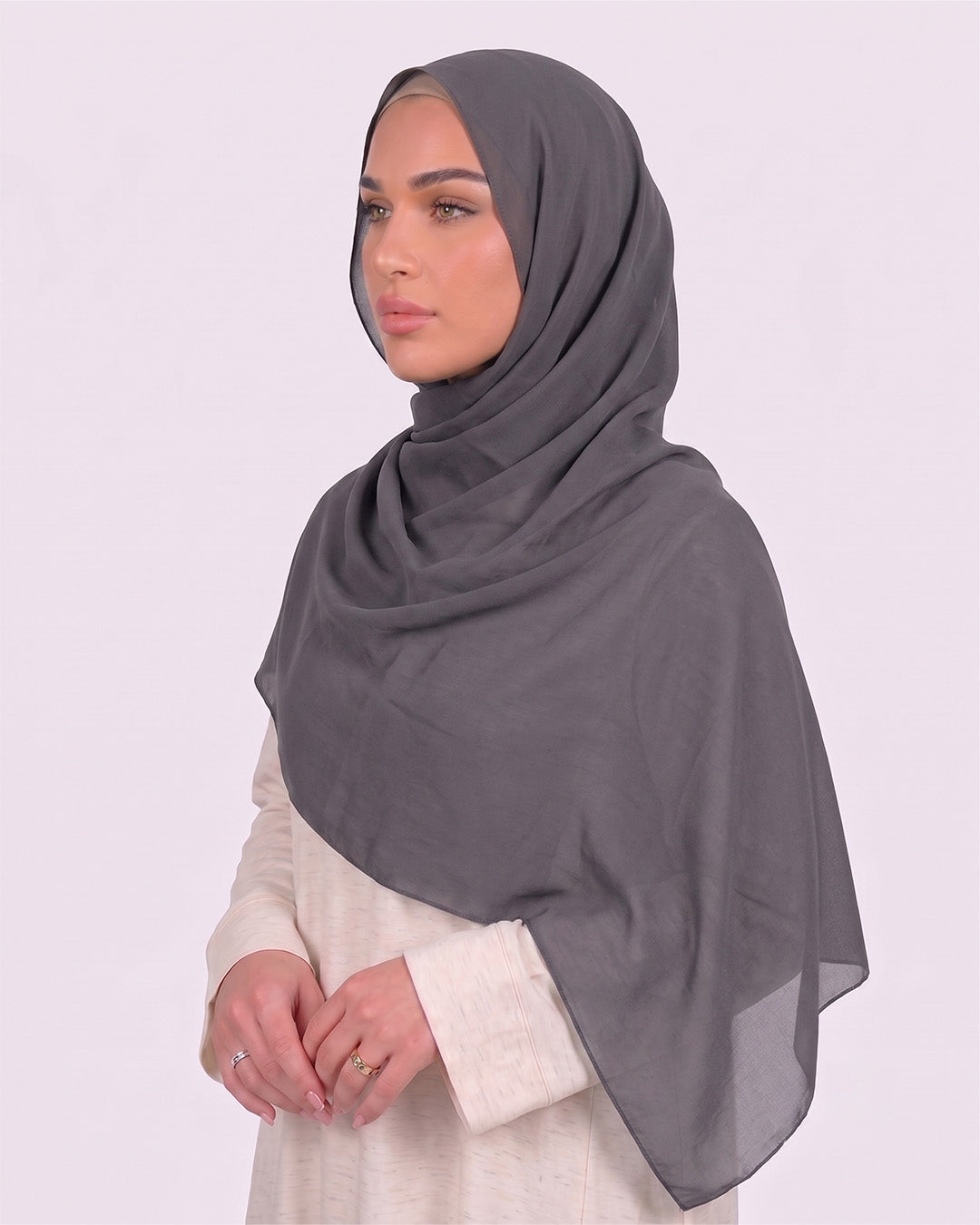 Model wearing a lightweight, dark gray chiffon hijab wrapped elegantly over a beige long-sleeved dress.