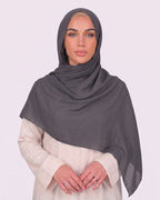 Model wearing a lightweight, dark gray chiffon hijab wrapped elegantly over a beige long-sleeved dress.