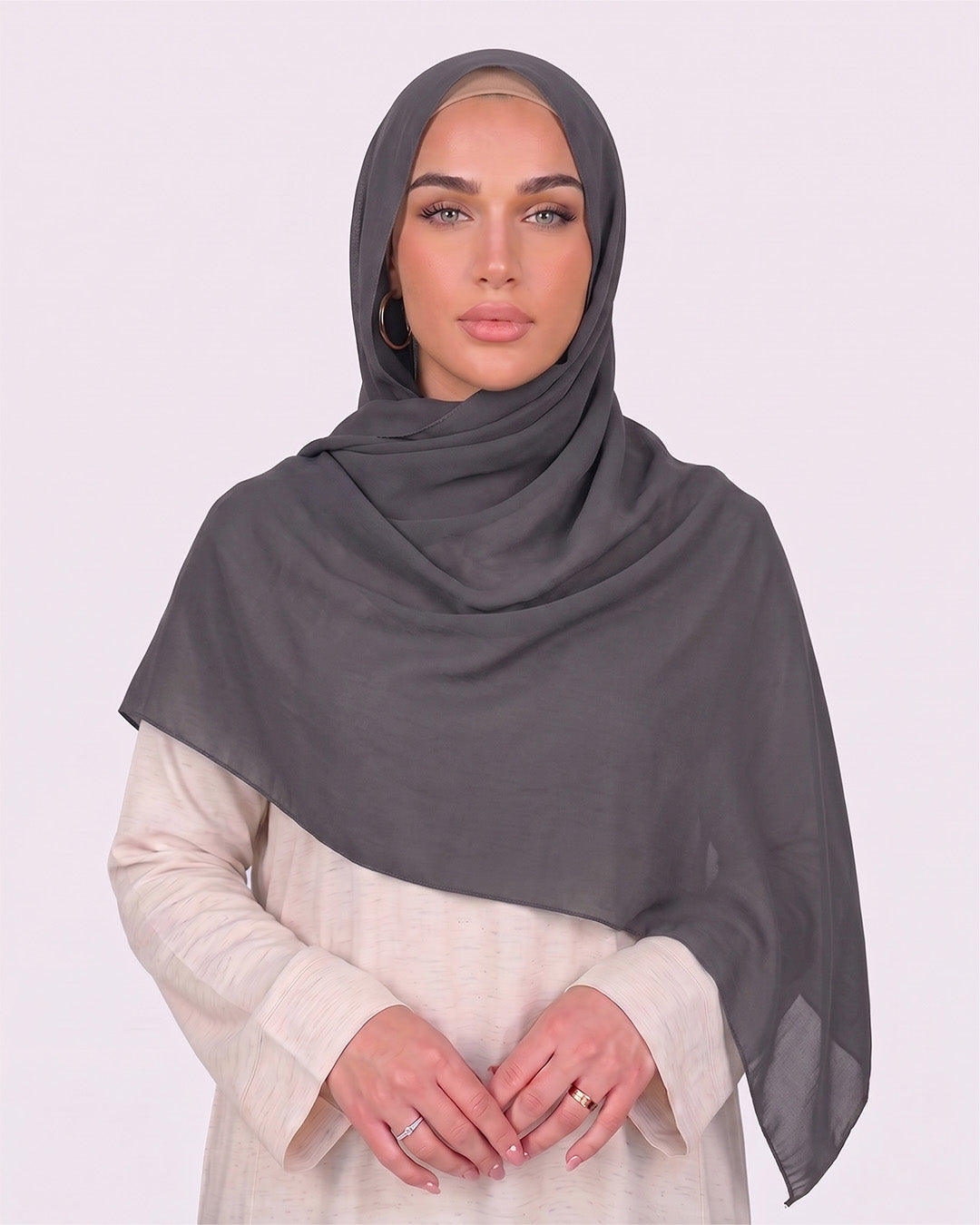 Model wearing a lightweight, dark gray chiffon hijab wrapped elegantly over a beige long-sleeved dress.