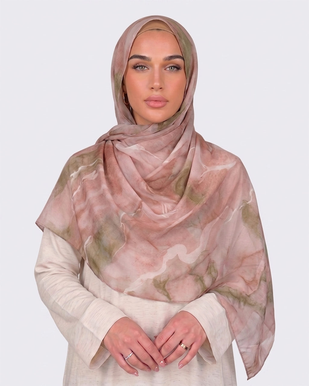 A woman wearing a soft dusty rose and blush pink printed modal hijab with fine marble veins of sage and olive green, paired with a cream outfit.