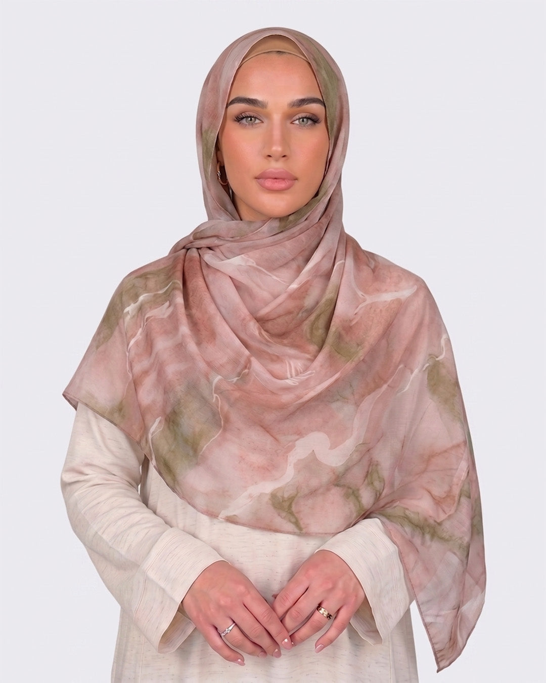 A woman wearing a soft dusty rose and blush pink printed modal hijab with fine marble veins of sage and olive green, paired with a cream outfit.