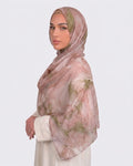 A woman wearing a soft dusty rose and blush pink printed modal hijab with fine marble veins of sage and olive green, paired with a cream outfit.