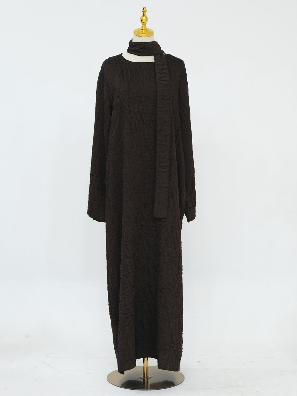 A long-sleeve, floor-length dark brown textured knit dress with a high mock neck and a matching draped scarf, displayed on a mannequin against a white studio background.