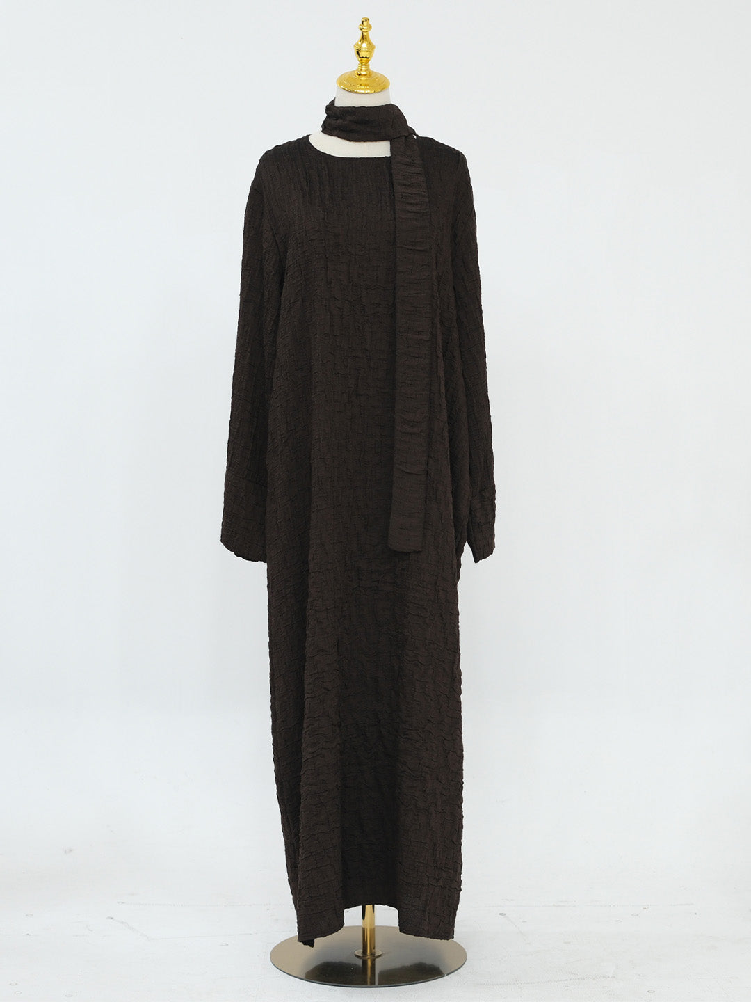 A long-sleeve, floor-length dark brown textured knit dress with a high mock neck and a matching draped scarf, displayed on a mannequin against a white studio background.