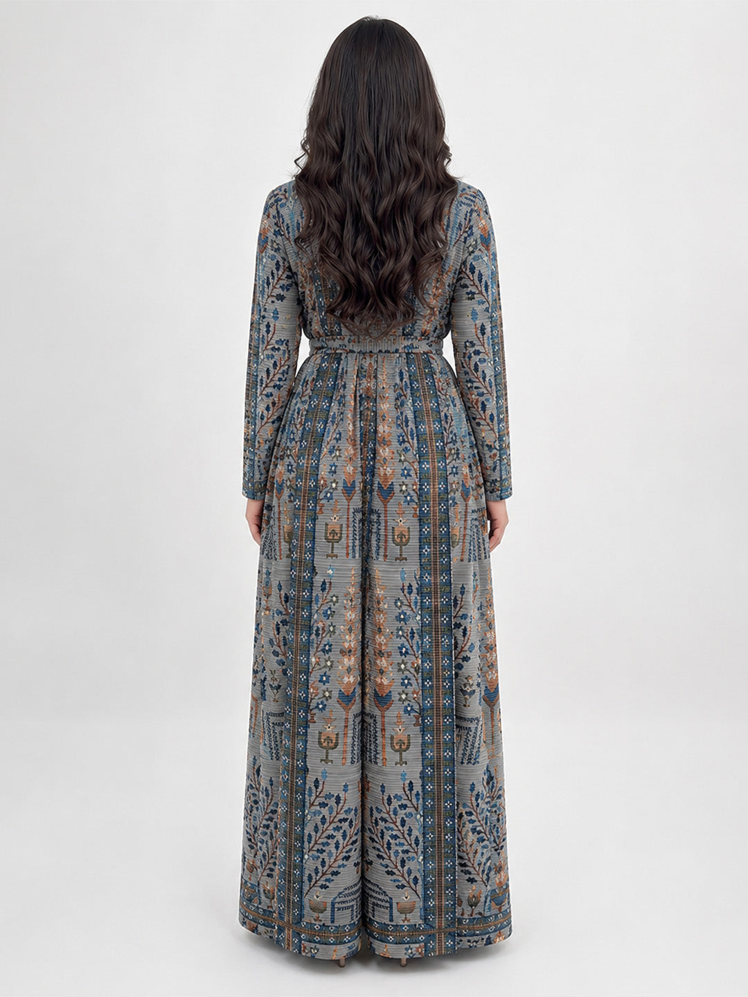 A woman viewed from the back wearing a long-sleeved maxi dress with an intricate blue, gray, and beige patterned print, set against a plain light gray studio background.