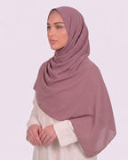 Model wearing a lightweight, dusty muave chiffon hijab wrapped elegantly over a beige long-sleeved dress.