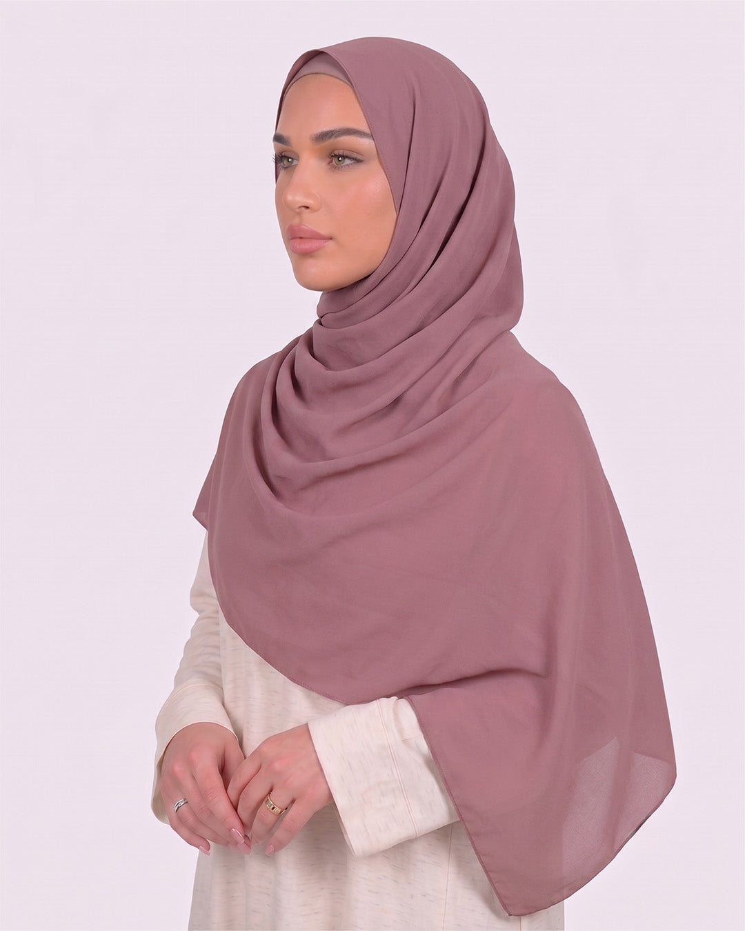 Model wearing a lightweight, dusty muave chiffon hijab wrapped elegantly over a beige long-sleeved dress.