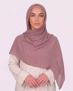 Model wearing a lightweight, dusty muave chiffon hijab wrapped elegantly over a beige long-sleeved dress.