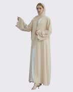 Woman wearing a beige abaya with intricate designs on a white background