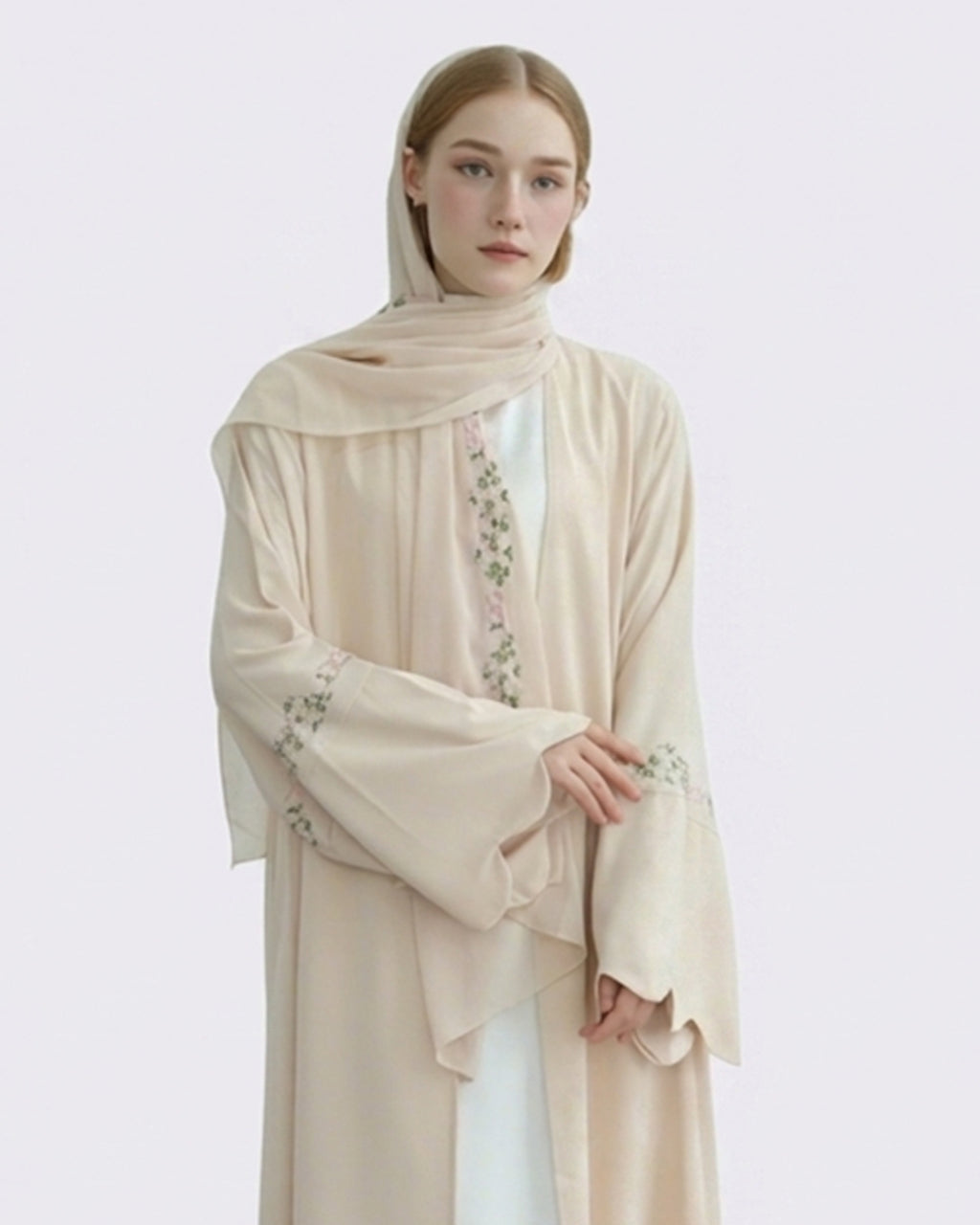 Woman wearing a beige embroidered abaya on a light gray background