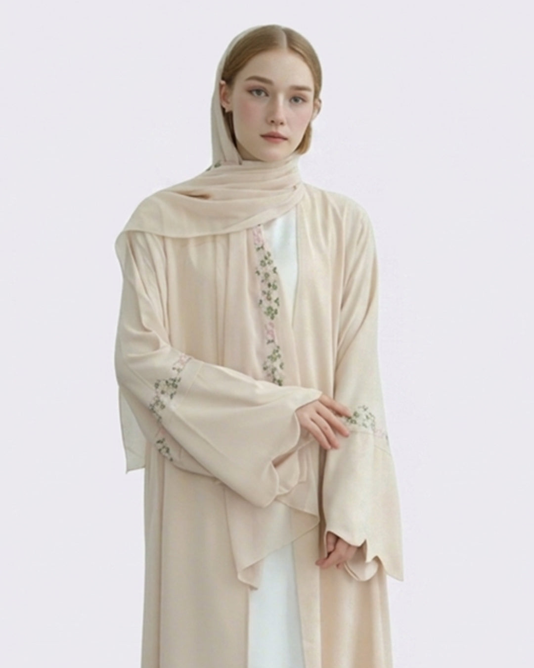 Woman wearing a beige embroidered abaya on a light gray background