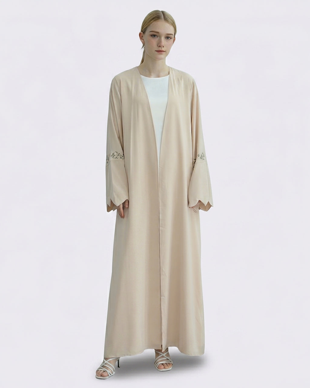 Woman wearing a beige abaya with floral embroidery on a white background