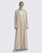 Woman wearing a beige abaya with floral embroidery on a white background
