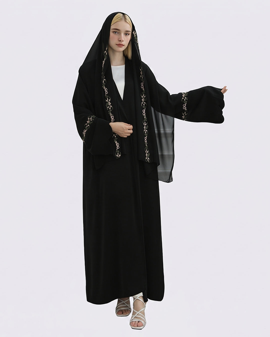 Woman wearing a black abaya with gold embroidery on a white background