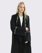 Woman wearing a black abaya with floral embroidery on a light gray background