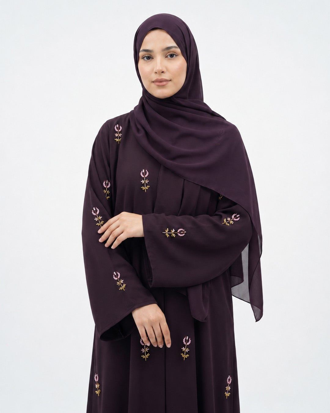 Woman wearing a dark purple abaya with gold embroidery on a white background
