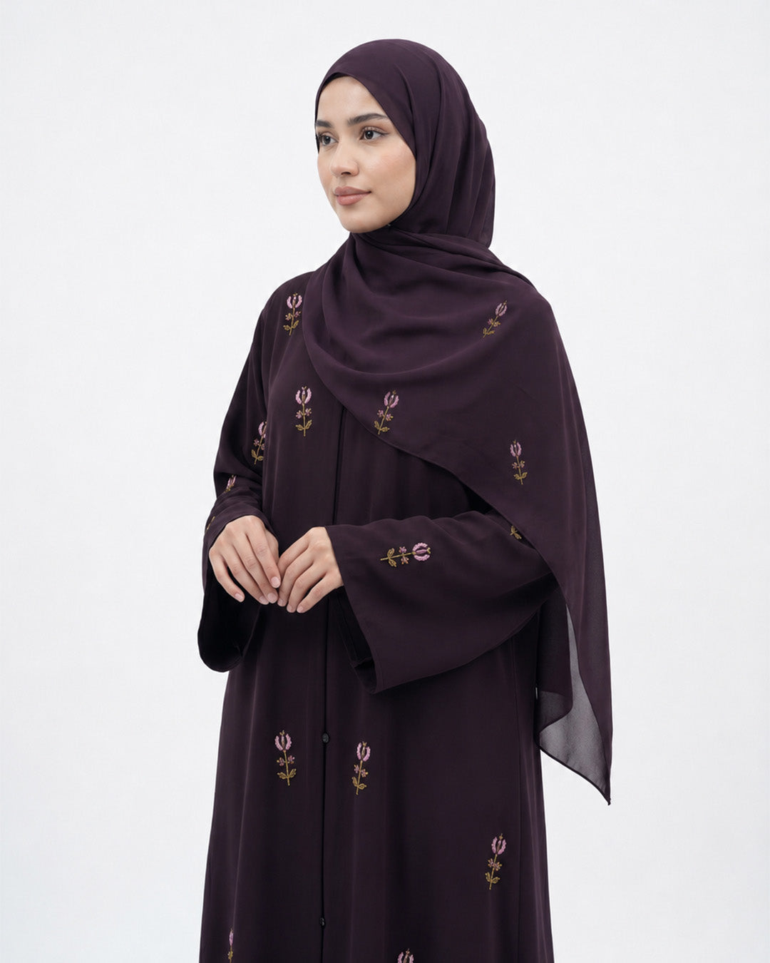 Woman wearing a dark purple abaya with floral embroidery on a white background