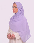 Model wearing a lightweight, light purple chiffon hijab wrapped elegantly over a beige long-sleeved dress.