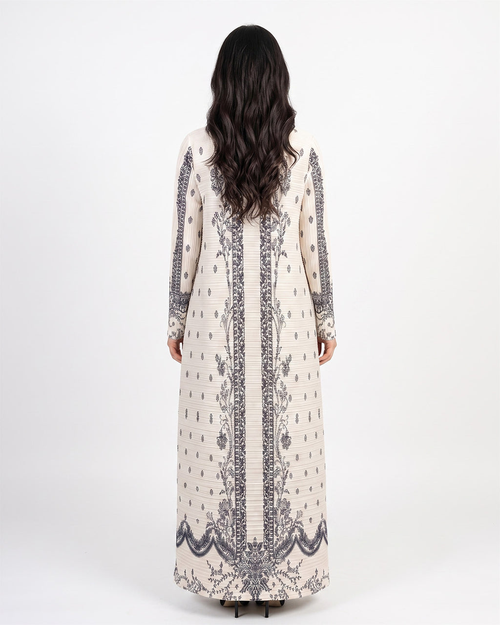 A woman viewed from the back wearing a long cream-colored kaftan dress with dark gray and black floral embroidery and vertical border details, set against a plain white studio background.