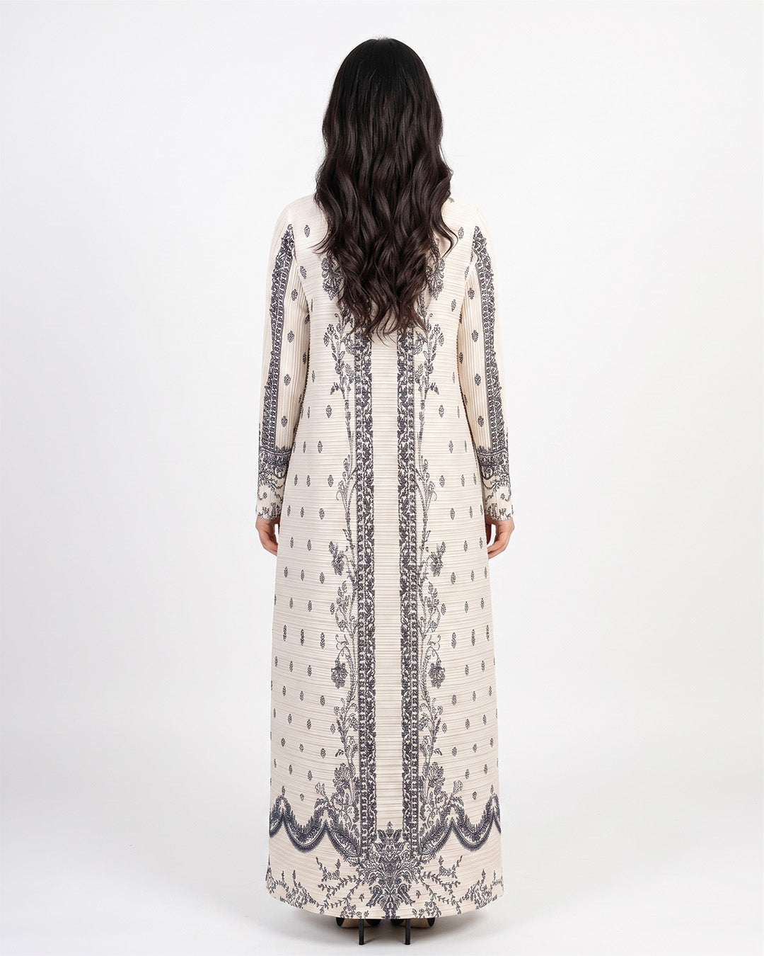 A woman viewed from the back wearing a long cream-colored kaftan dress with dark gray and black floral embroidery and vertical border details, set against a plain white studio background.