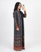 A woman takes a mirror selfie wearing a long navy blue printed kaftan dress with intricate red, gold, and beige patterns, set against a plain white studio background.