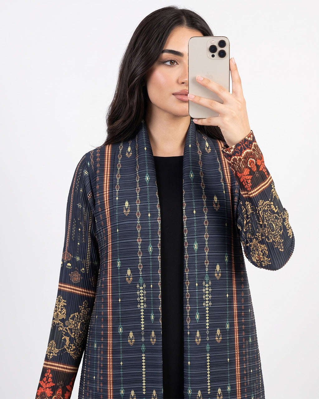 A woman takes a mirror selfie wearing a navy blue open-front cardigan with vertical geometric patterns and ornate gold and red floral embroidery on the cuffs, over a black top.