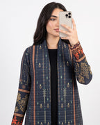 A woman takes a mirror selfie wearing a navy blue open-front cardigan with vertical geometric patterns and ornate gold and red floral embroidery on the cuffs, over a black top.