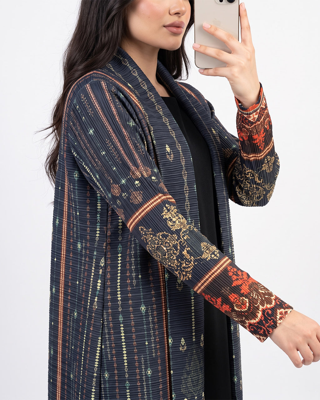 A woman takes a mirror selfie wearing a dark navy open-front cardigan with vertical stripes and ornate gold and red patterned sleeves, layered over a black top.