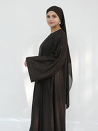 A woman modeling a dark brown abaya with matching headscarf, shown from the side against a light gray studio background.
