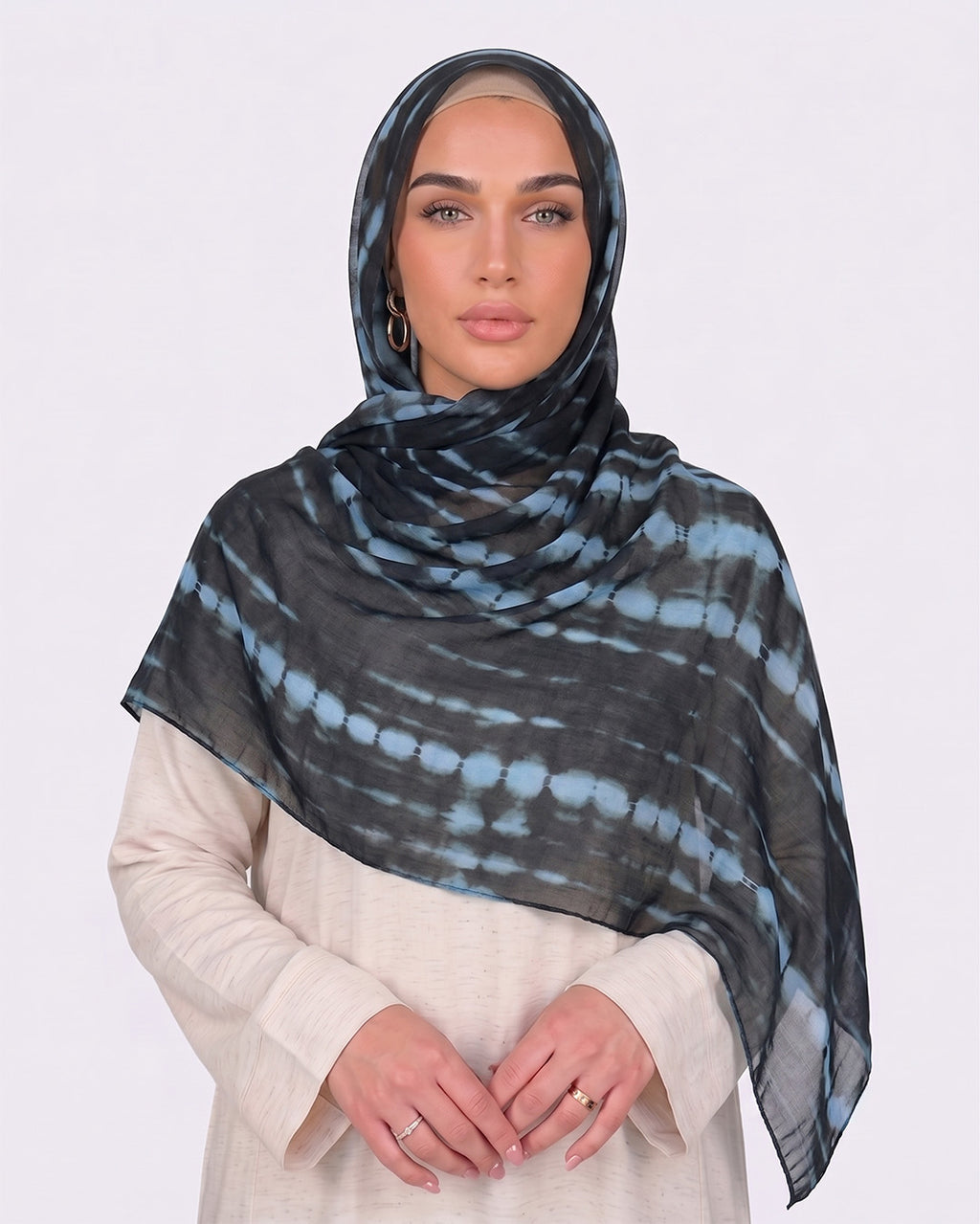 A woman wearing a modern black printed modal hijab with horizontal tie-dye stripes in steel blue and slate grey, paired with a cream outfit.