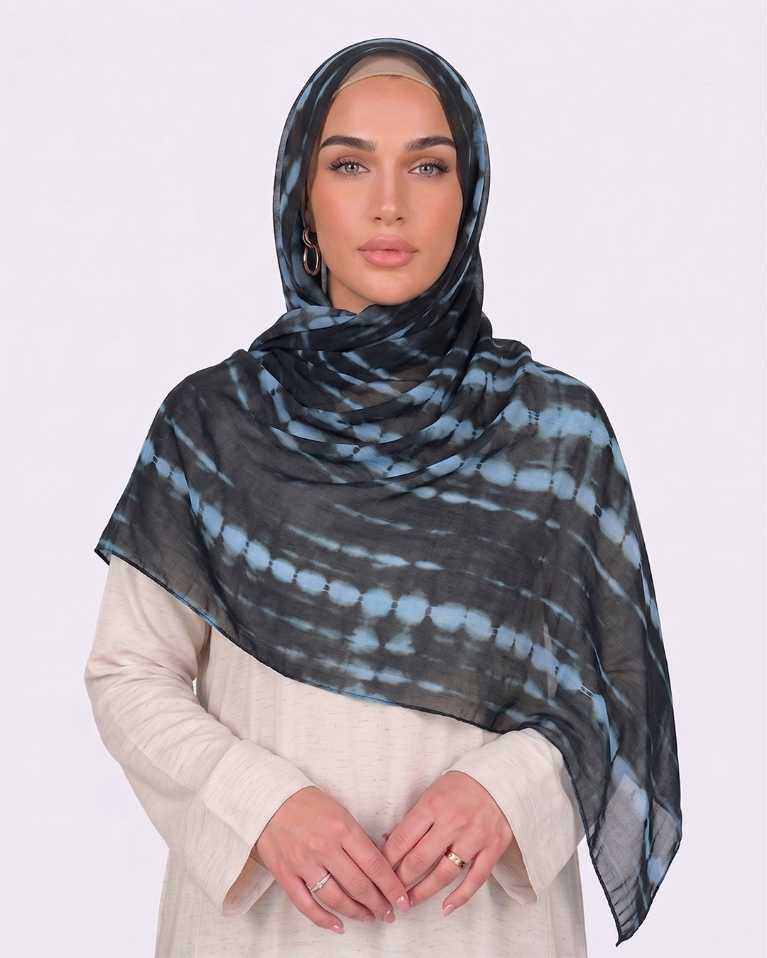 A woman wearing a modern black printed modal hijab with horizontal tie-dye stripes in steel blue and slate grey, paired with a cream outfit.