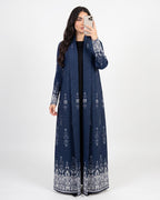 A woman takes a mirror selfie wearing a long navy blue open-front abaya with intricate white and silver floral embroidery on the sleeves and hem, set against a plain light gray background.