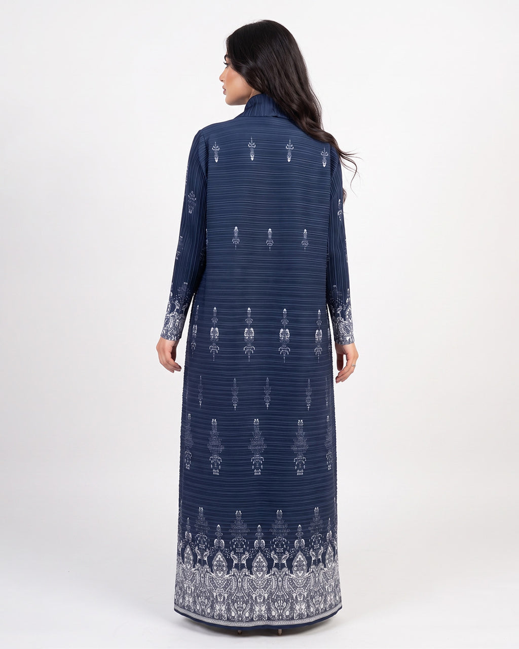 A woman shown from the back wearing a long navy blue dress with white vertical stripes and white printed patterns, photographed against a plain light gray studio background.