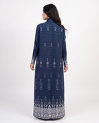 A woman shown from the back wearing a long navy blue dress with white vertical stripes and white printed patterns, photographed against a plain light gray studio background.