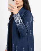 A woman takes a mirror selfie wearing a navy blue open-front cardigan with white floral embroidery on the cuffs and hem, layered over a black top against a plain white background.