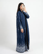 A woman takes a mirror selfie wearing a long navy blue open-front abaya with intricate white floral embroidery on the sleeves, hem, and front opening, photographed against a plain white studio background.