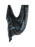 A lightweight black scarf with a blue tie-dye shibori pattern, draped against a solid white background.