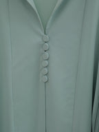 Close-up of a pale sage green garment with a V-neckline and a vertical row of five round buttons down the center front.