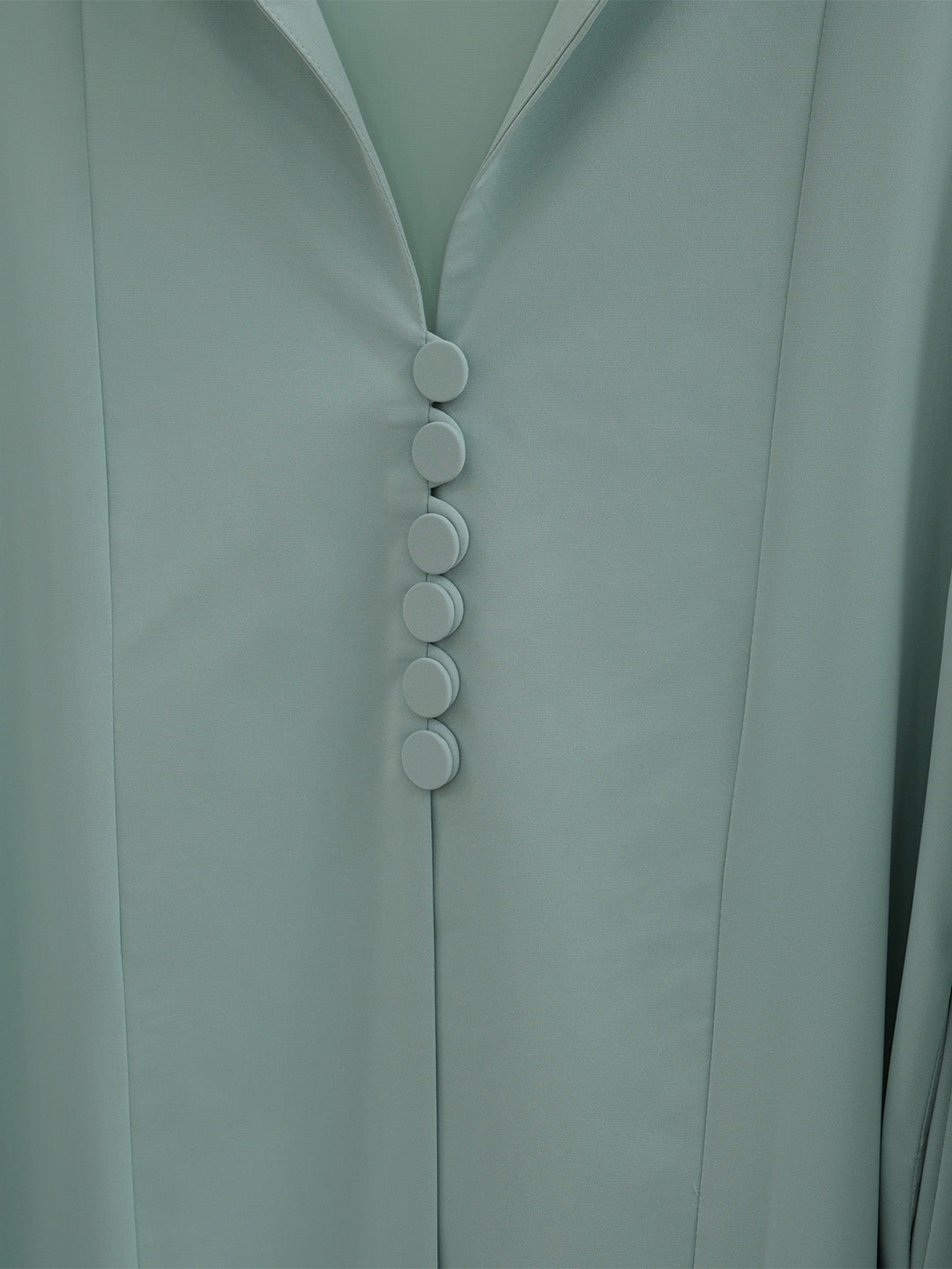 Close-up of a pale sage green garment with a V-neckline and a vertical row of five round buttons down the center front.