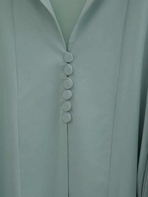 Close-up of a pale sage green garment with a V-neckline and a vertical row of five round buttons down the center front.