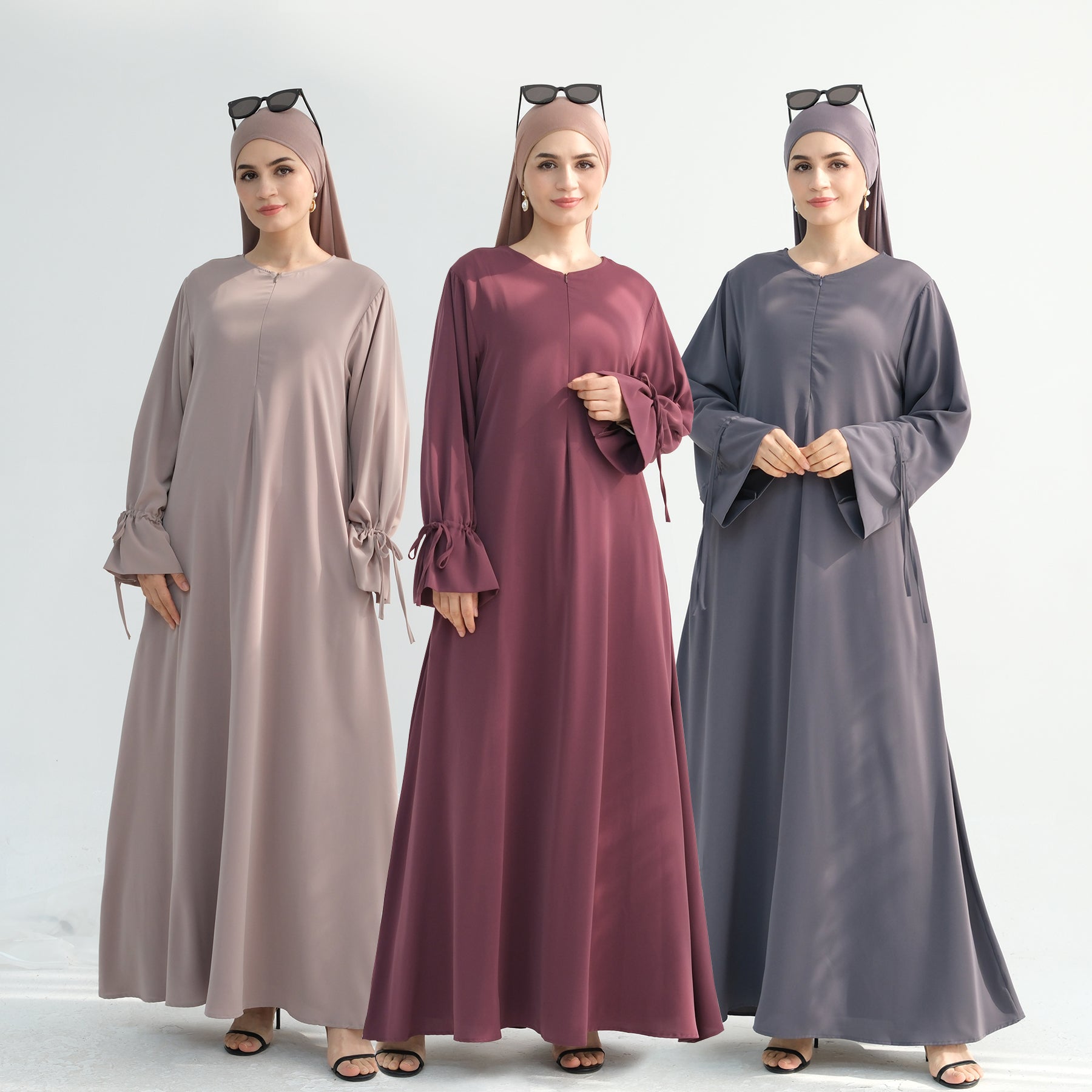 Three women wearing long, floor-length dresses in beige, purple, and gray on a white background.
