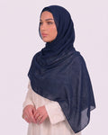 Model wearing a lightweight, navy blue chiffon hijab wrapped elegantly over a beige long-sleeved dress.