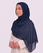 Model wearing a lightweight, navy blue chiffon hijab wrapped elegantly over a beige long-sleeved dress.
