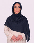 Model wearing a lightweight, navy blue chiffon hijab wrapped elegantly over a beige long-sleeved dress.